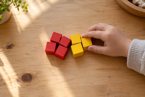 A hand bringing red and yellow wooden counting blocks together on a table