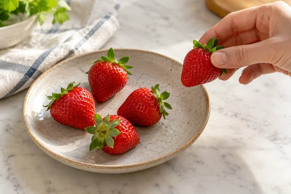 A hand lifting a strawberry from a plate