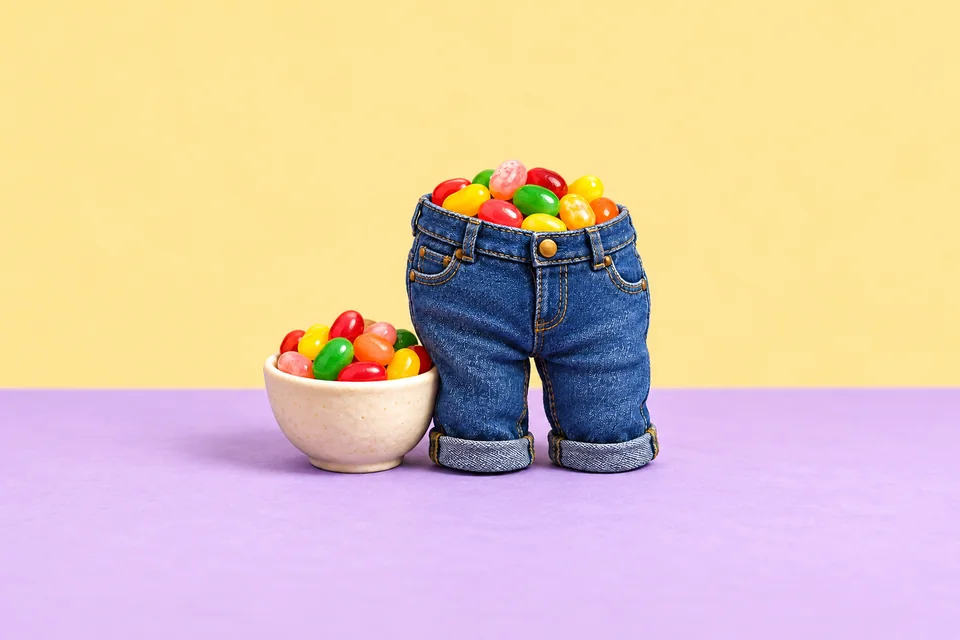 An imaginary pair of small blue jeans filled with colourful jelly beans beside a bowl of sweets