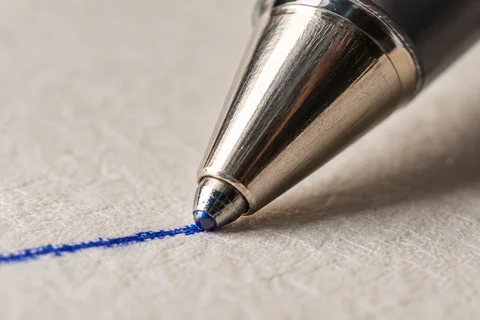 A macro view of a ballpoint pen tip making a blue ink line on textured paper