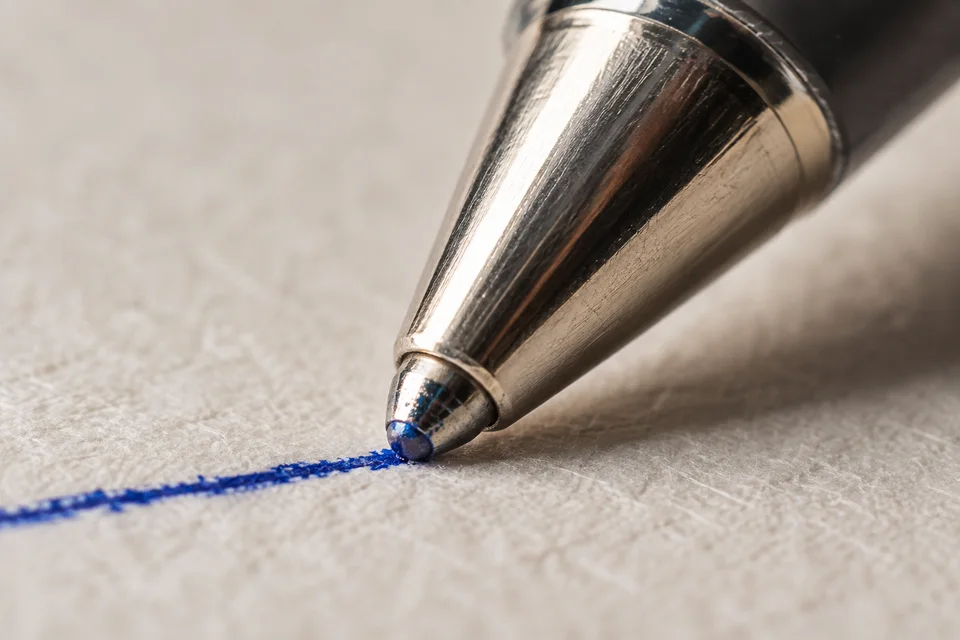 A macro view of a ballpoint pen tip making a blue ink line on textured paper
