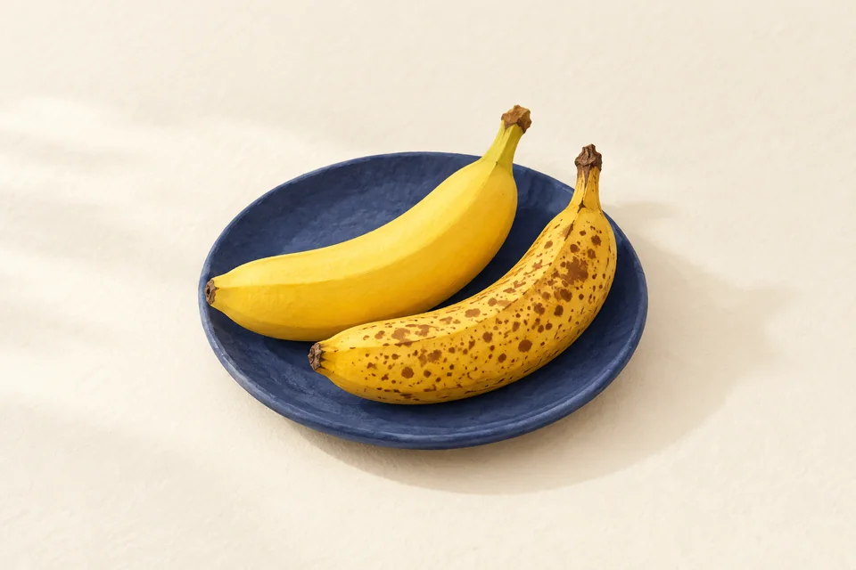 Two yellow bananas on an indigo plate, one plain and one with scattered brown speckles